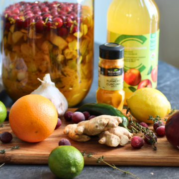 Fire cider in glass jar and all ingredients on a cutting board.