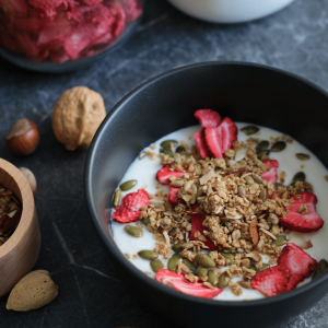 Black bowl with homemade yogurt, granola and freeze dried strawberries.