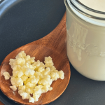 Wooden spoon with kefir grains beside a pint jar of milk kefir.