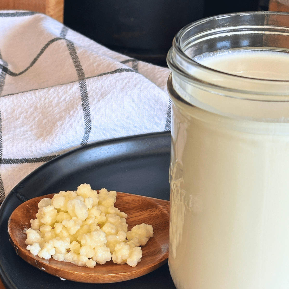 Pint jar of milk kefir beside a wooden spoon with kefir grains.