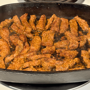 Donair seasoned beef strips in a cast iron pan.