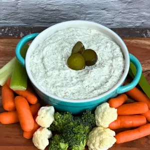 Dill pickle dip in dish surrounded by veggies.