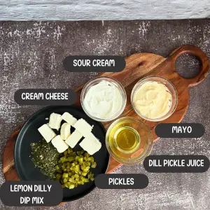 All ingredients for the dill pickle dip in bowls on a decorative cutting board.