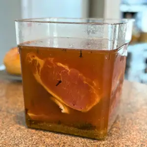 Piece of pork loin in a clear container with salt brine.