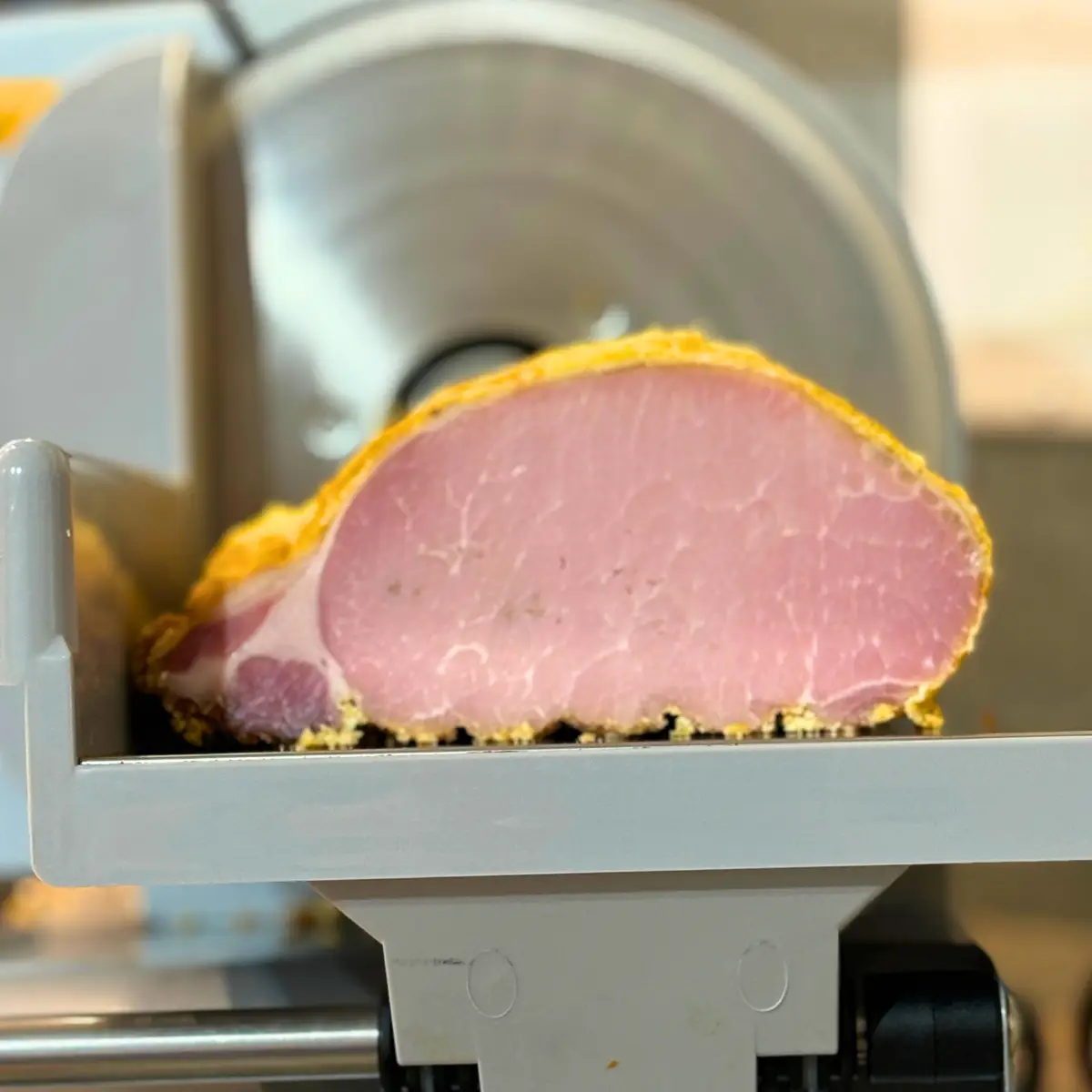 Cured and smoked piece of homemade Canadian Bacon on a meat slicer.