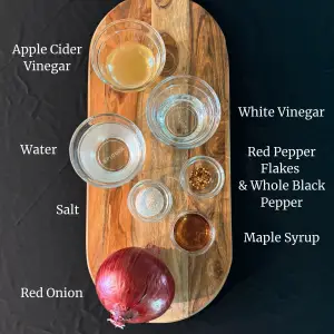 Ingredients needed for making pickled red onions on a wooden cutting board. 