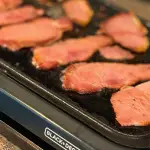 Back bacon frying on a griddle.