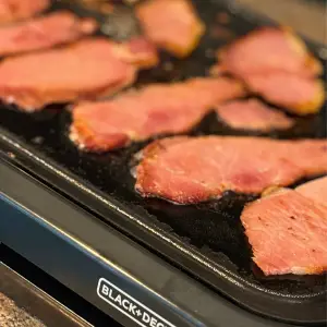 Back bacon frying on a griddle.