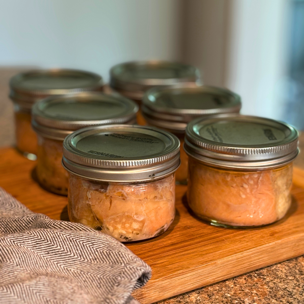 Jars of canned salmon cooling on a cutting board.