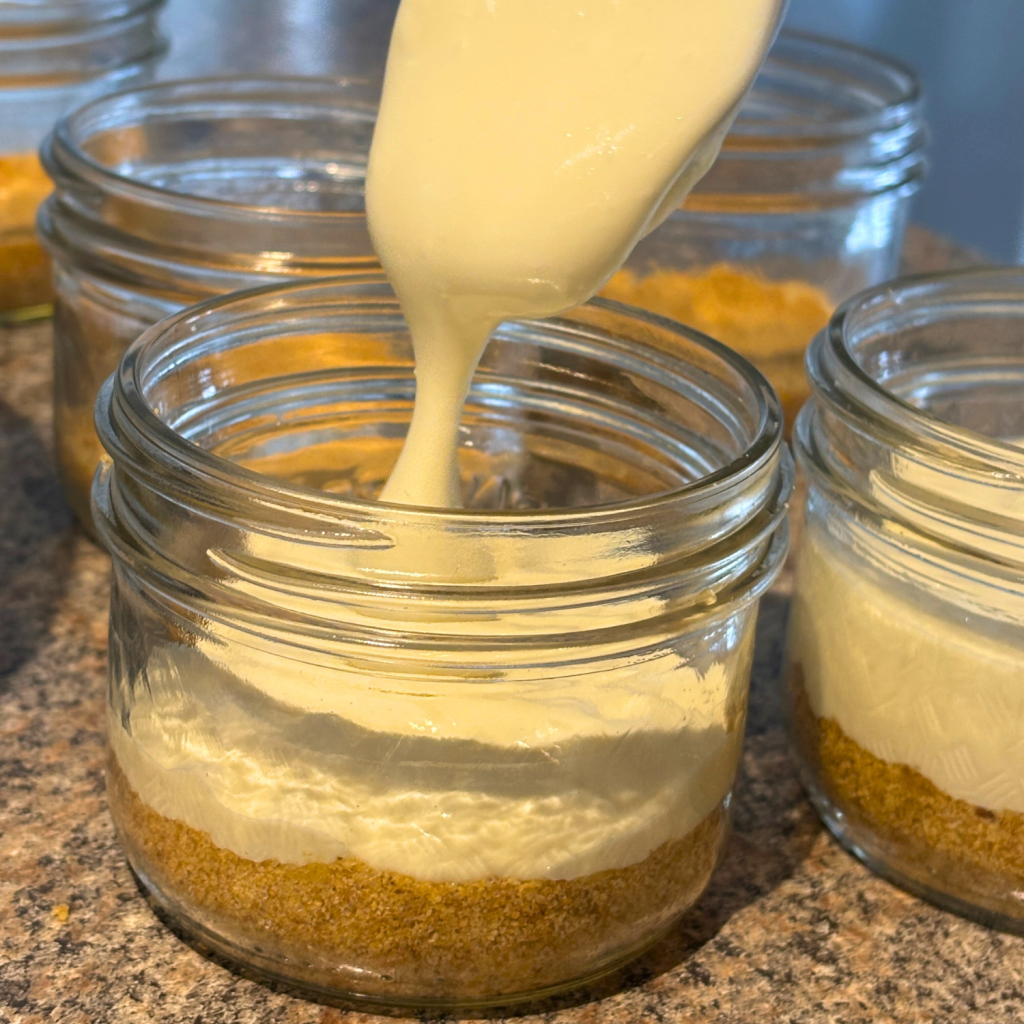 Spooning cheesecake batter on top of graham crust bottom in a mason jar.