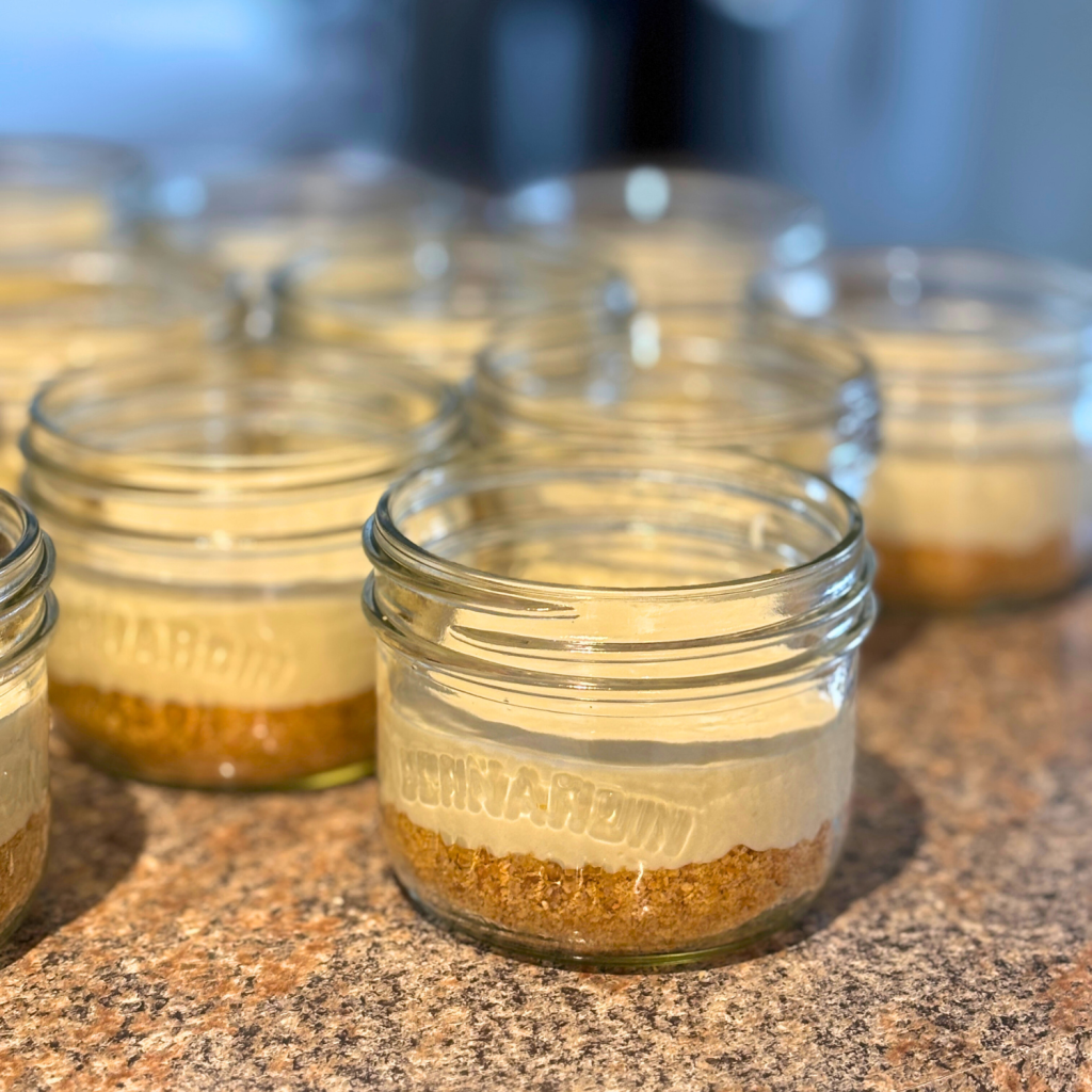 Mason jars with crust in bottom and cheesecake batter on top.