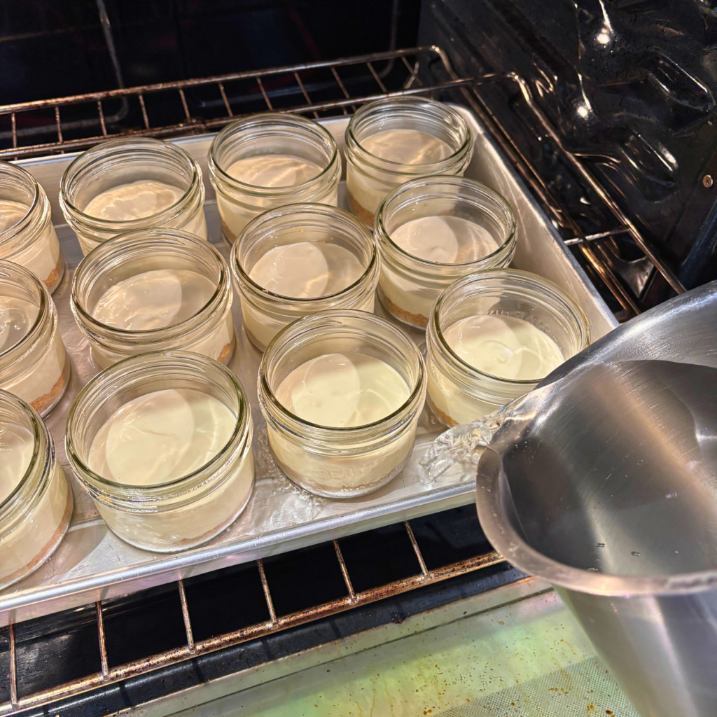 Pouring water into the baking dish halfway up the sides of the cheesecake jars.