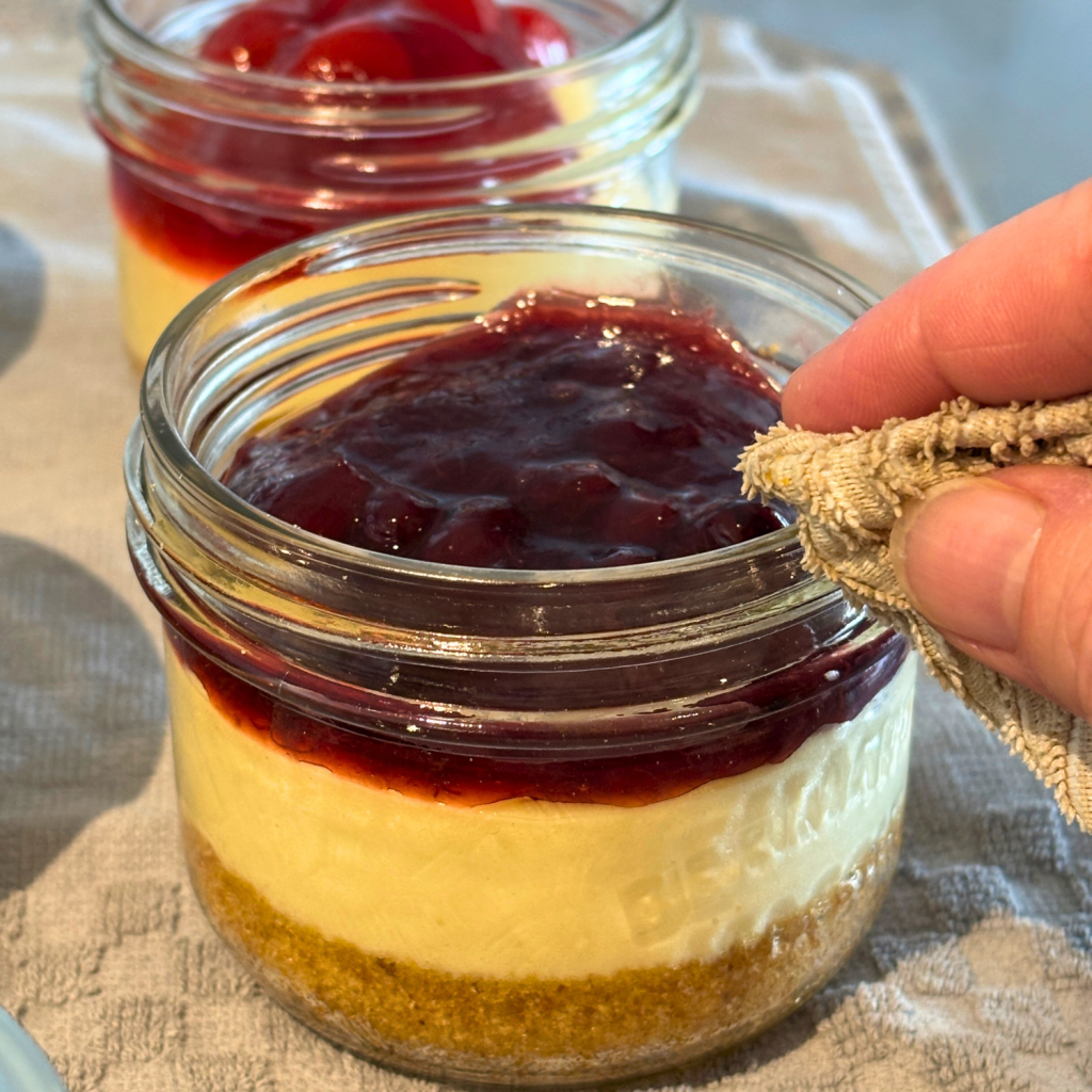 Wiping the rim of a cheesecake in a jar with a cloth.