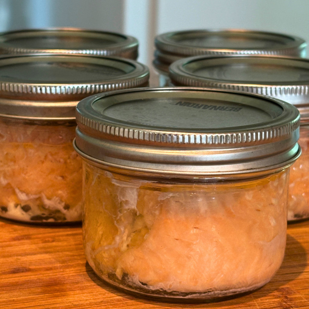 Jars of canned salmon on a wooden cutting board.