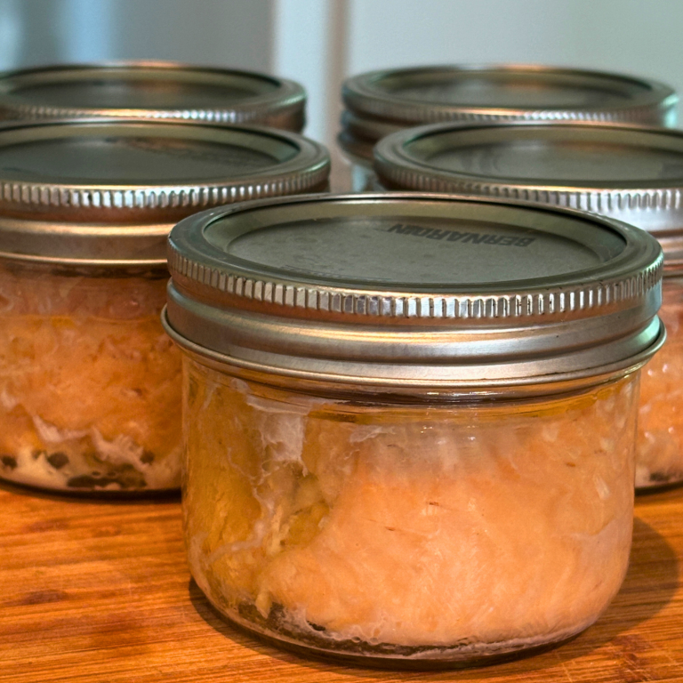 Jars of canned salmon on a wooden cutting board.