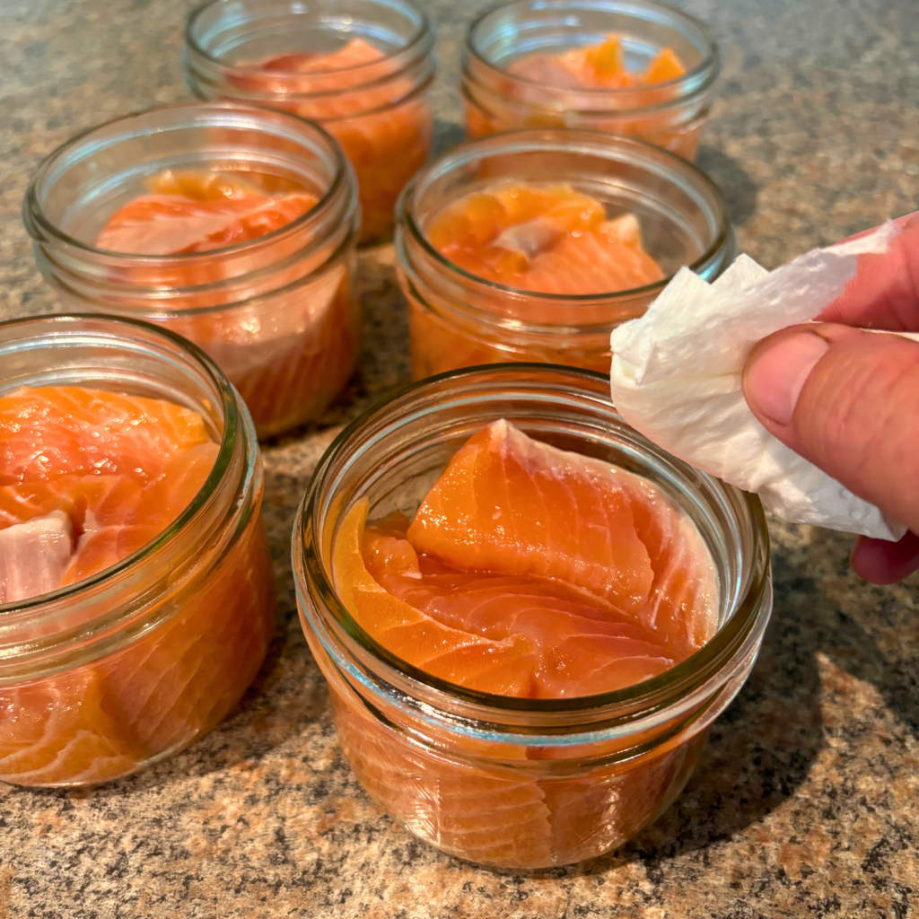 Salmon pieces packed into half pint canning jars.