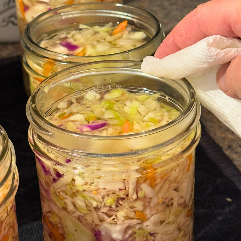 Wiping edges of pint jar full of coleslaw