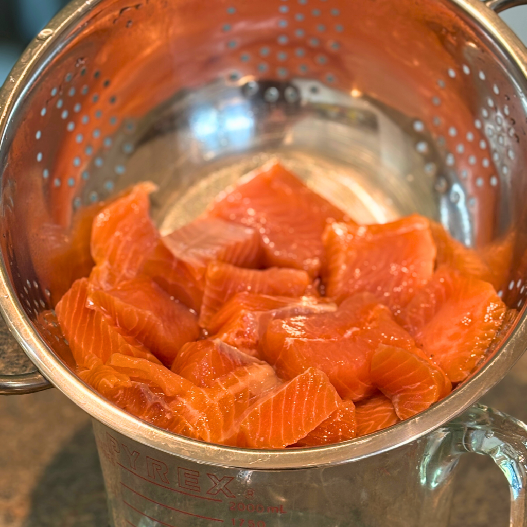Salmon pieces draining in a colander.