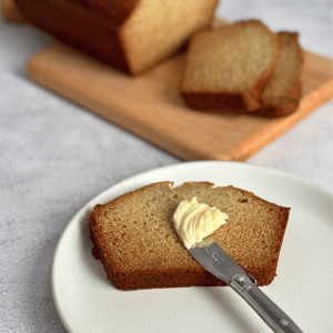 Banana Bread sliced on a cutting board and a piece of banana bread with a pad of butter and a knife.