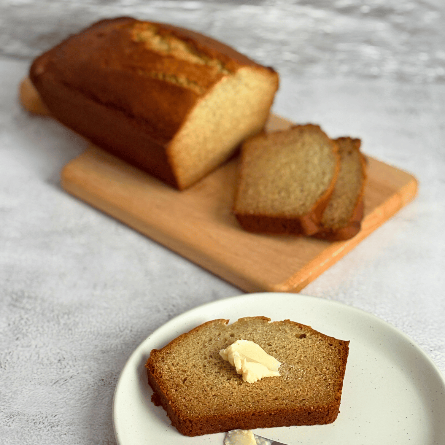 Banana Bread on a cutting and one slice has a pad of butter on it.