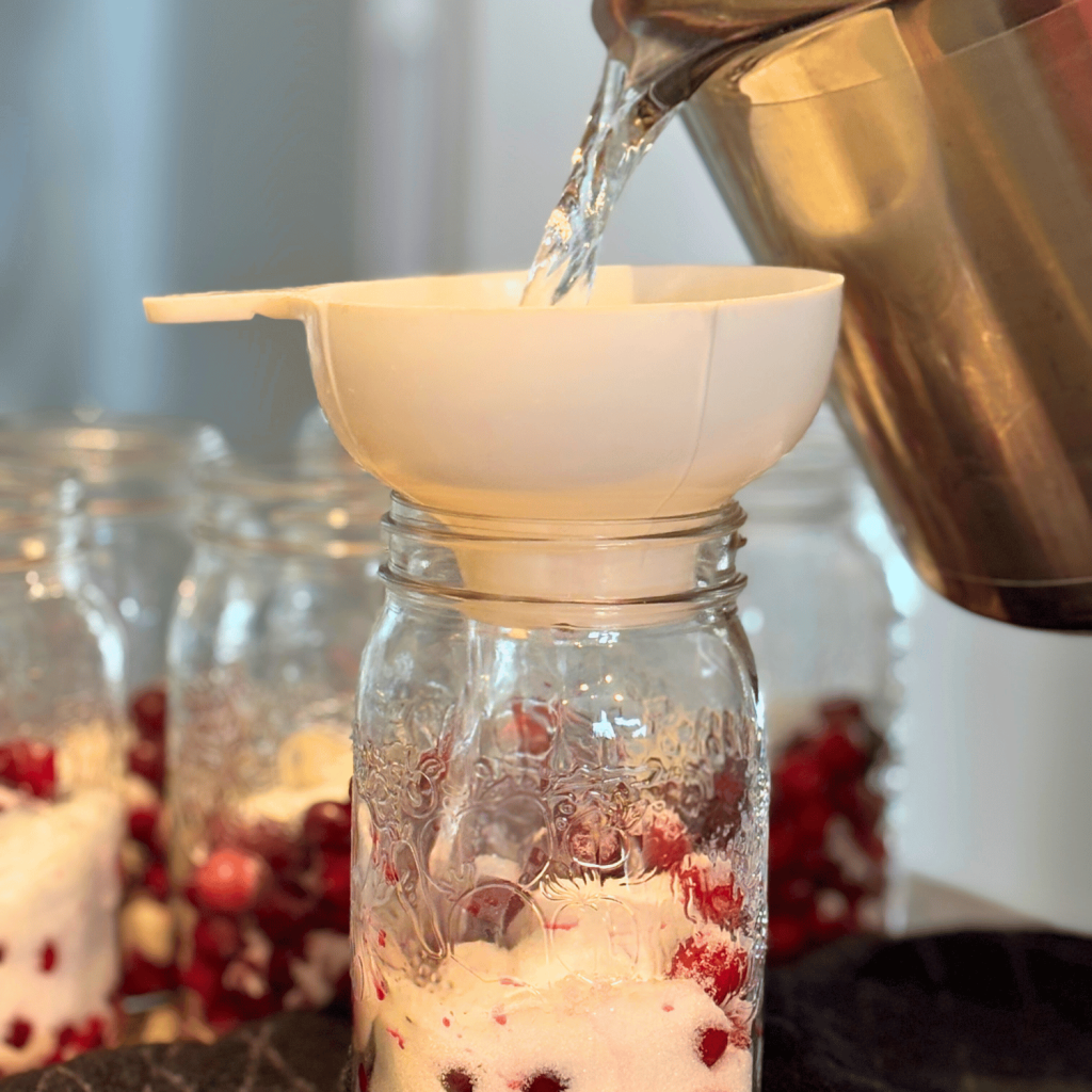 Pouring boiling water over cranberries and sugar in a quart jar.