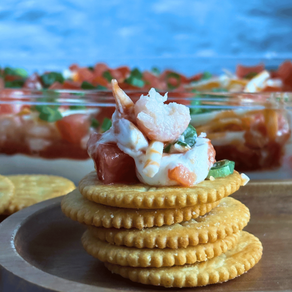 Layered Seafood Dip on top of a stack of Ritz crackers.