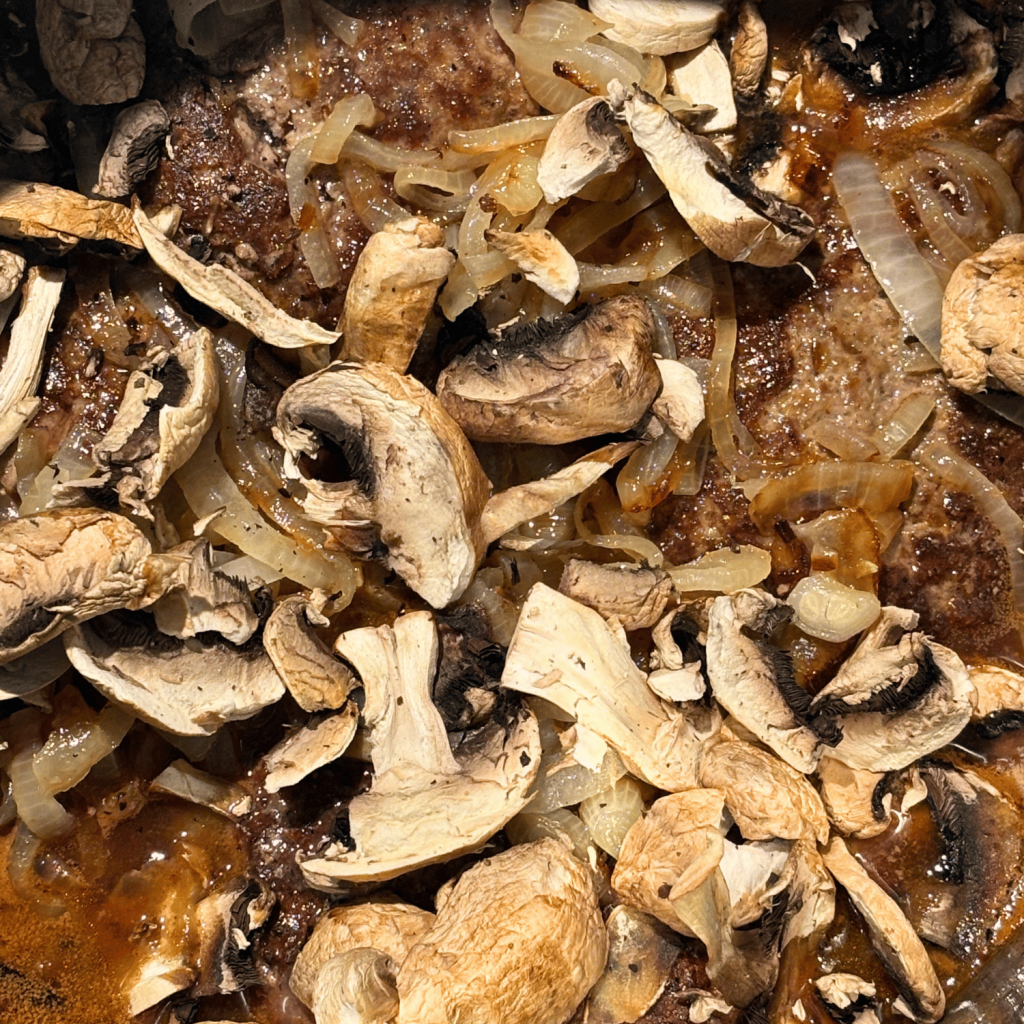 Sliced mushrooms adding on top of the browned beef patties in the Instant Pot.