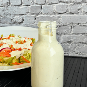 Bottle of creamy buttermilk blue cheese salad dressing with a bowl of lettuce salad in the background.