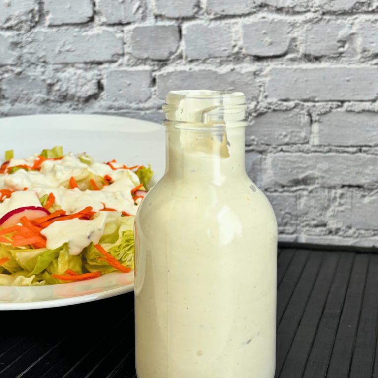 Bottle of creamy buttermilk blue cheese salad dressing with a bowl of lettuce salad in the background.