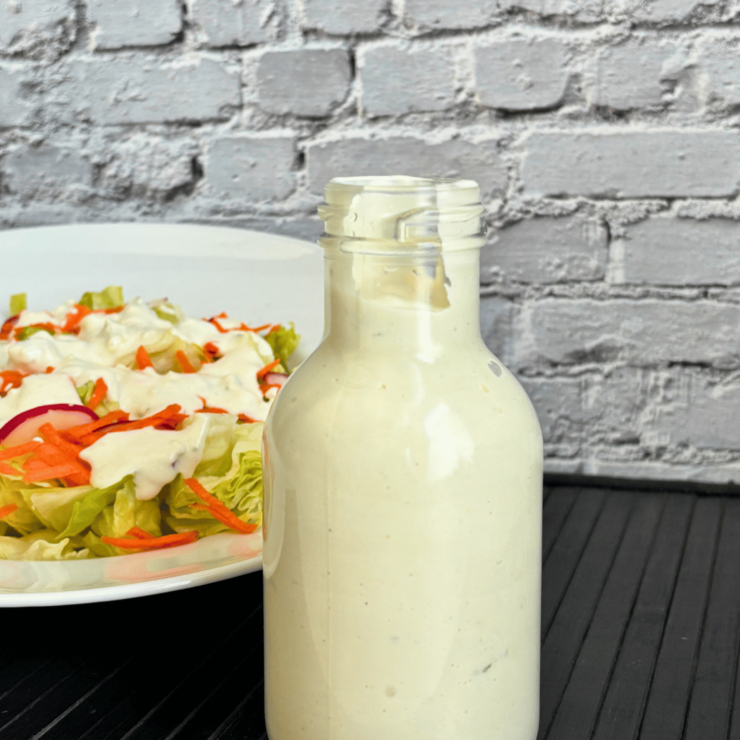 Bottle of creamy buttermilk blue cheese salad dressing with a bowl of lettuce salad in the background.