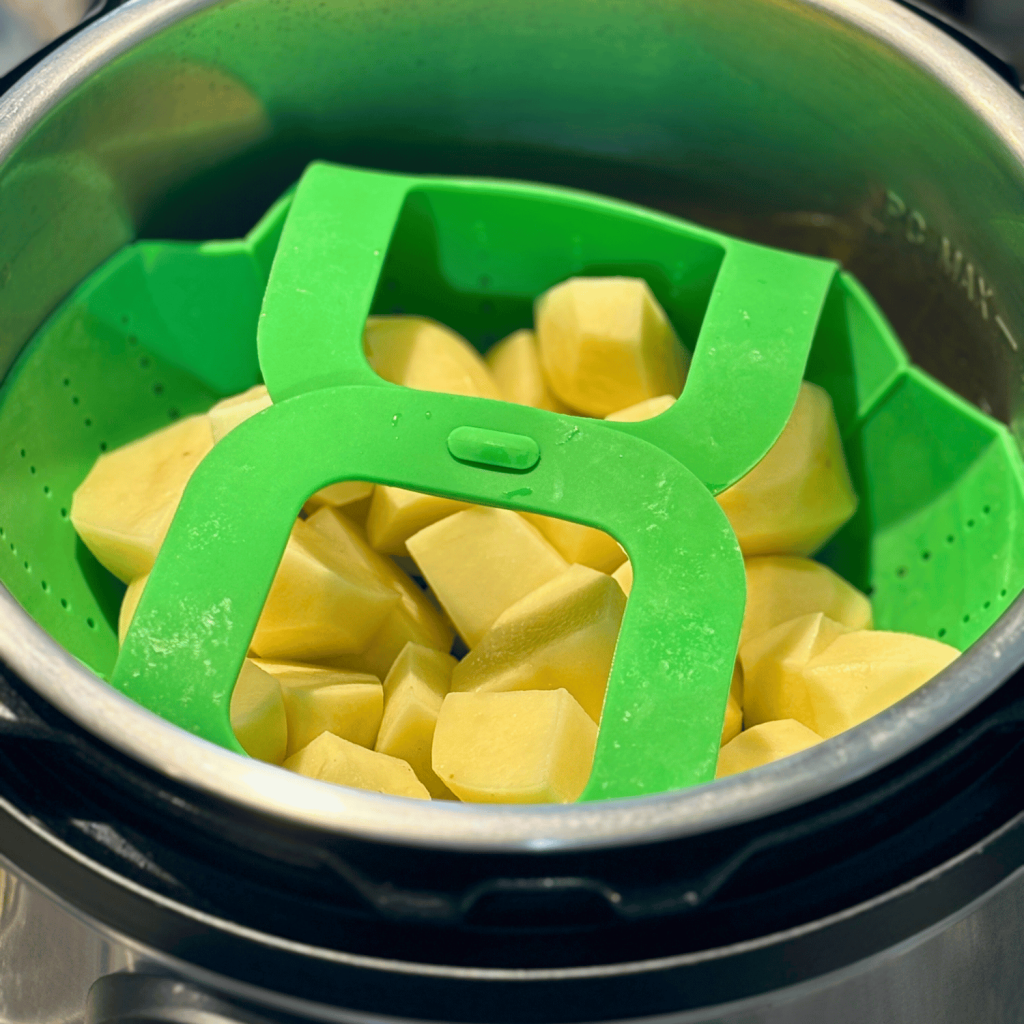 Cubed potatoes in a silicone basket put on top of beef patties inside the instant pot.
