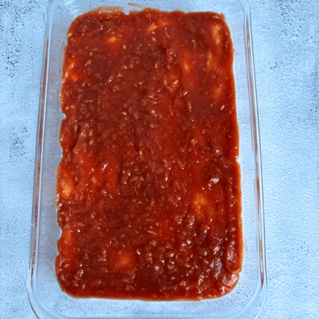 Cocktail sauce spread over the cream cheese layer in a glass dish.