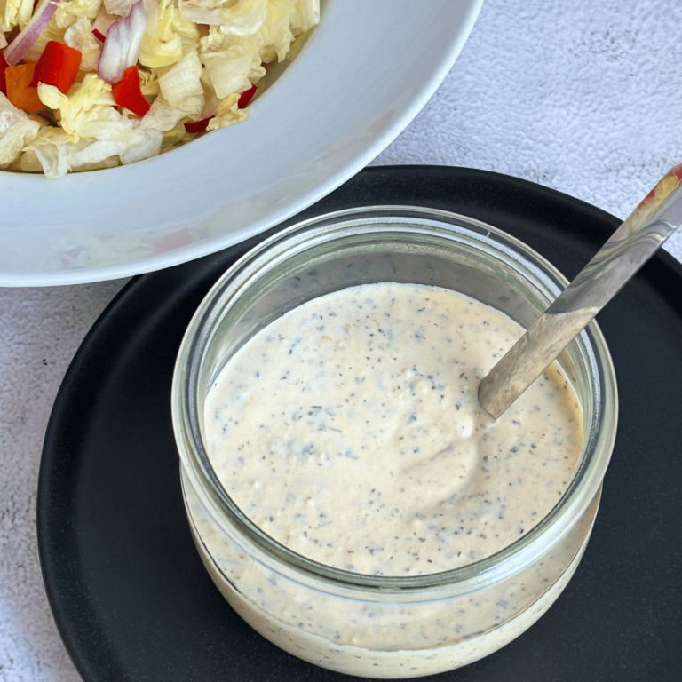 Creamy Italian dressing in a Weck jar next to a plate of toss salad.