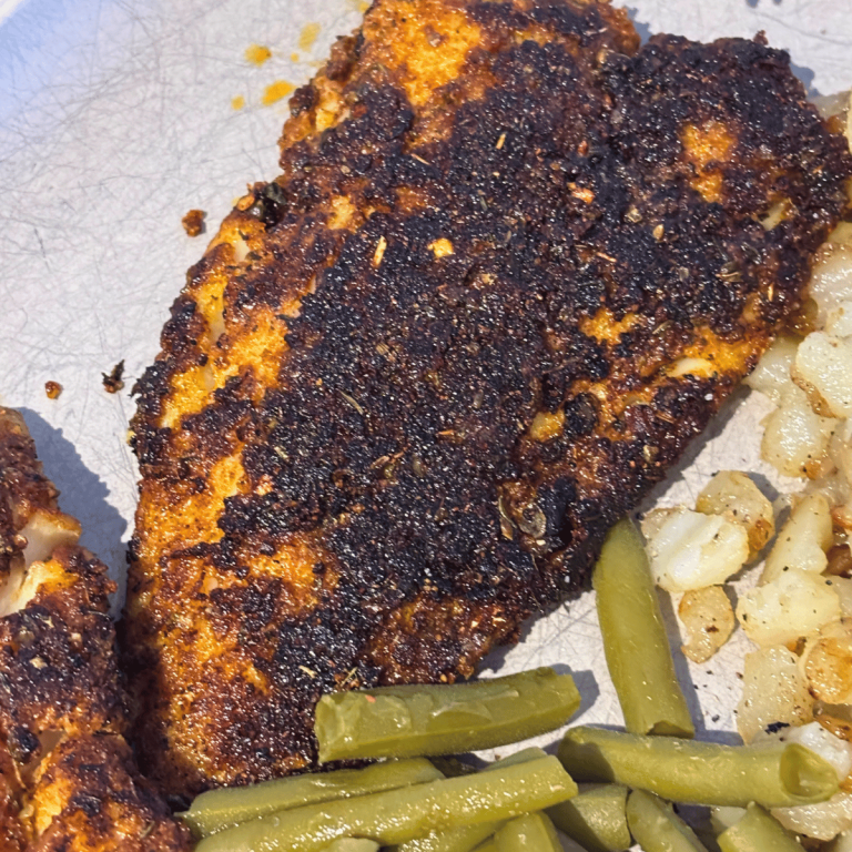 Piece of blackened fish on a plate with potatoes and green beans.