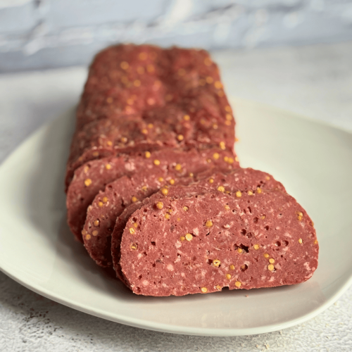 Homemade summer sausage on a white plate, some has been sliced.