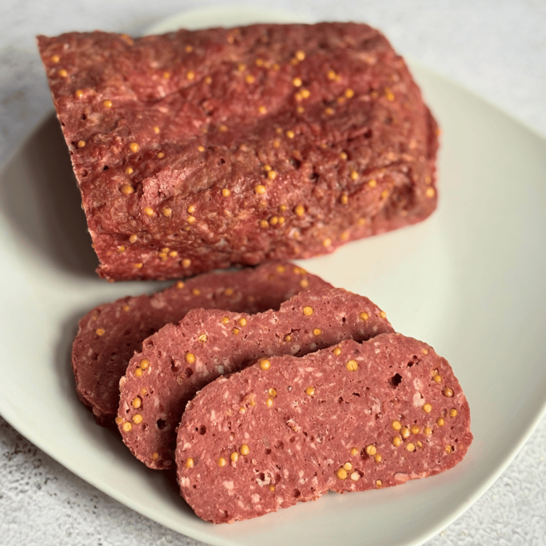 Homemade Summer Sausage with some sliced on a white plate.
