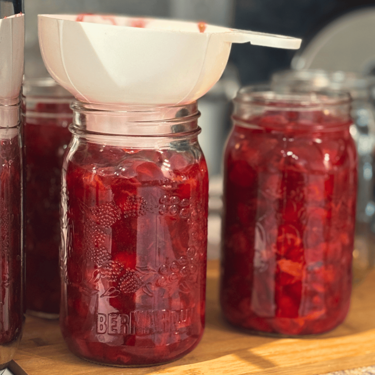 Homemade cherry pie filling being put into quart jars.