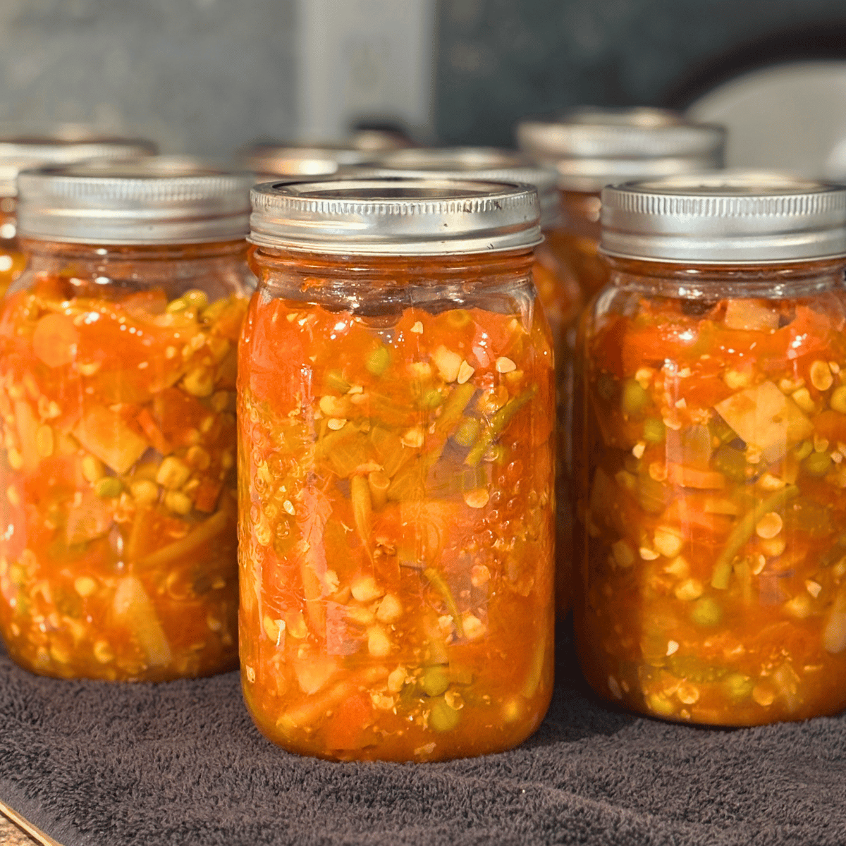 Jars of Canned Homemade Vegetable Soup on a black towel on the counter.