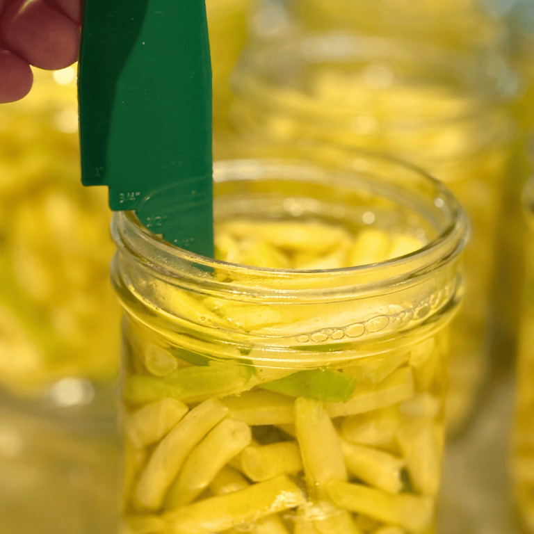 Jars filled with yellow beans and water with a headspace tool checking the headspace