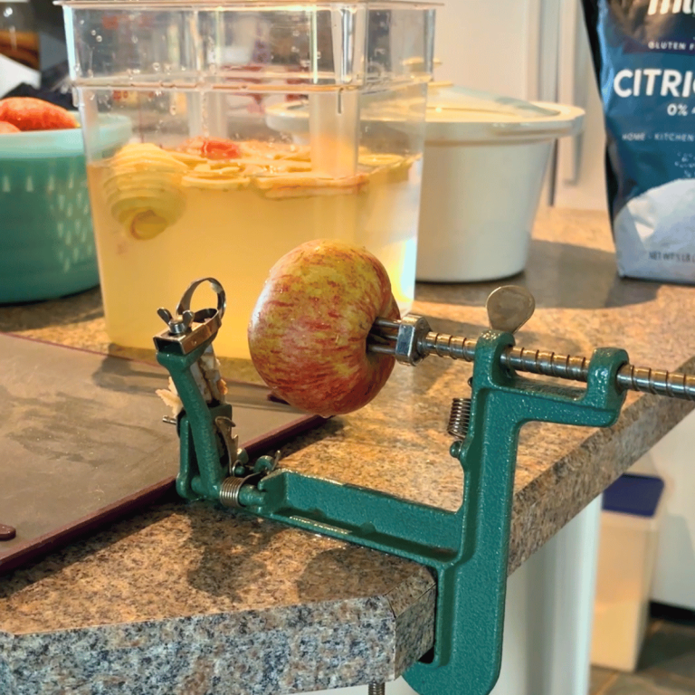 Apple core and slicing tool clamped to the counter for prepping apples for homemade apple pie filling.