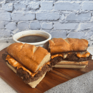 Beef Dip Sandwich cut into two pieces on a cutting board with a bowl of au jus