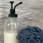 Homemade body wash in glass dispenser next to a loofa