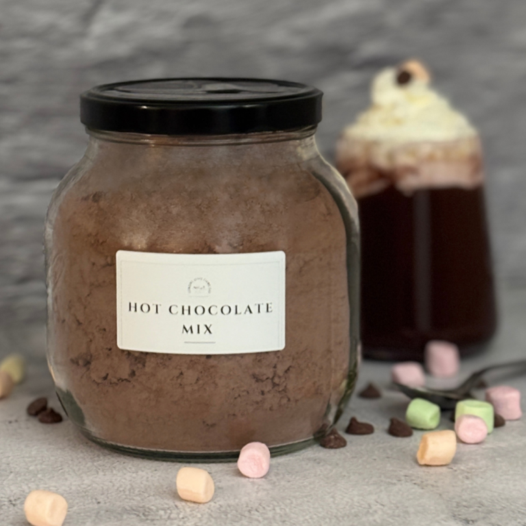 Homemade Hot Chocolate Mix in a glass jar with a cup of hot cocoa in the background