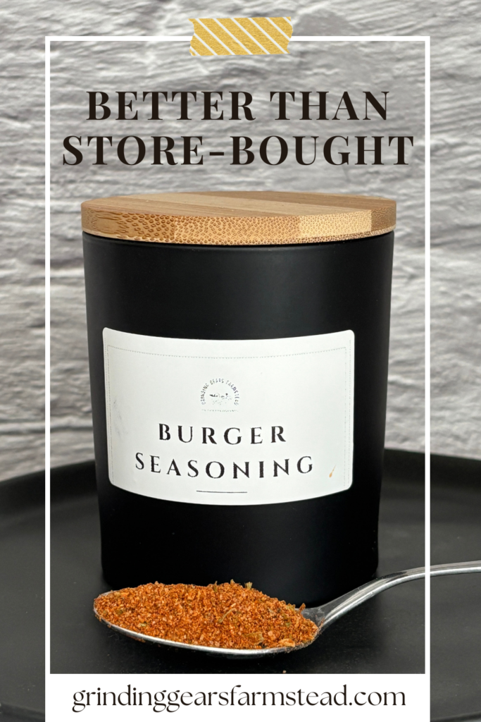 Homemade burger seasoning in a glass black jar with a bamboo lid and a spoon full of seasoning.