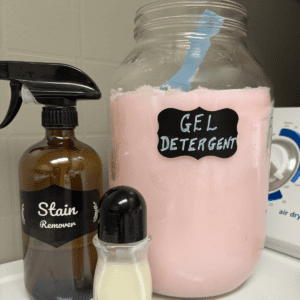 Glass jar of laundry gel detergent beside a glass spray stain remover and a roll on stain remover